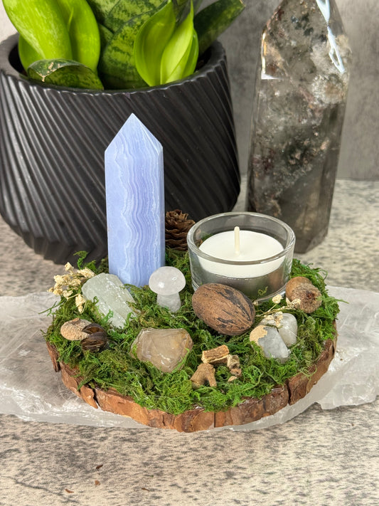 Mossy wreath with a candle, crystals, and stones on a stone surface.