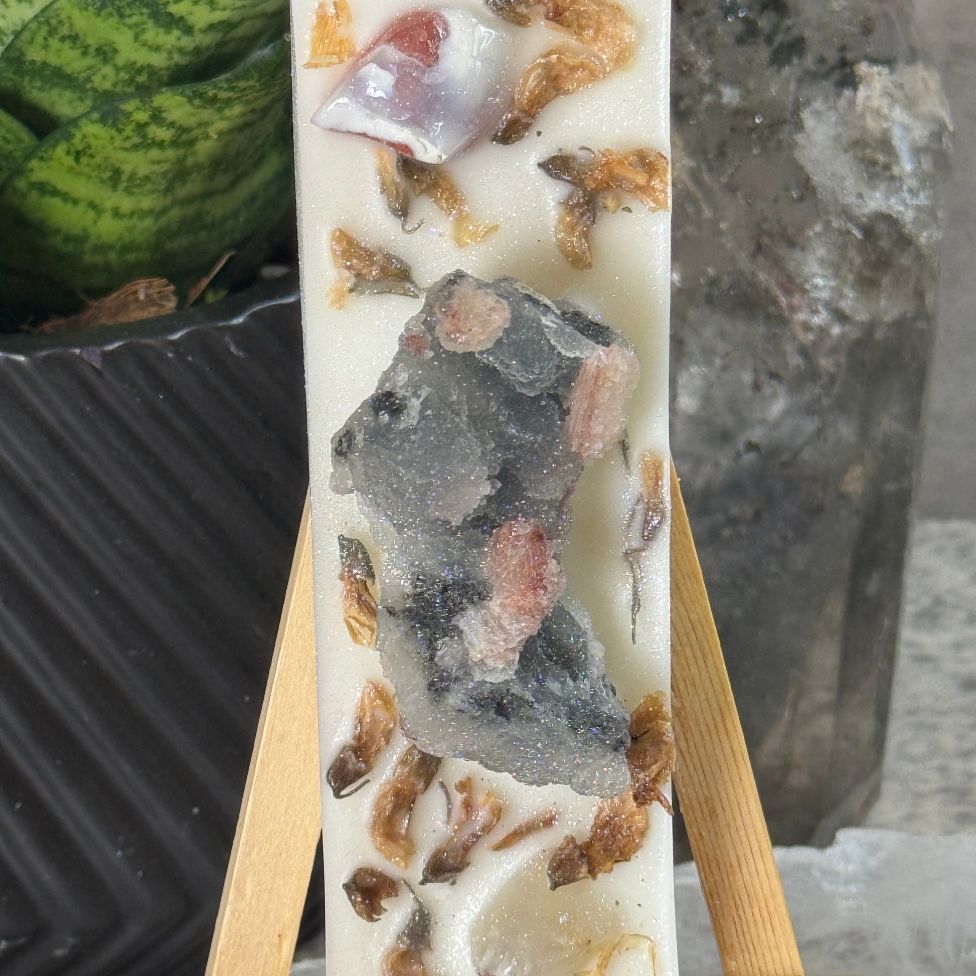 Decorative stone with embedded shells on a wooden stand against a natural rock background
