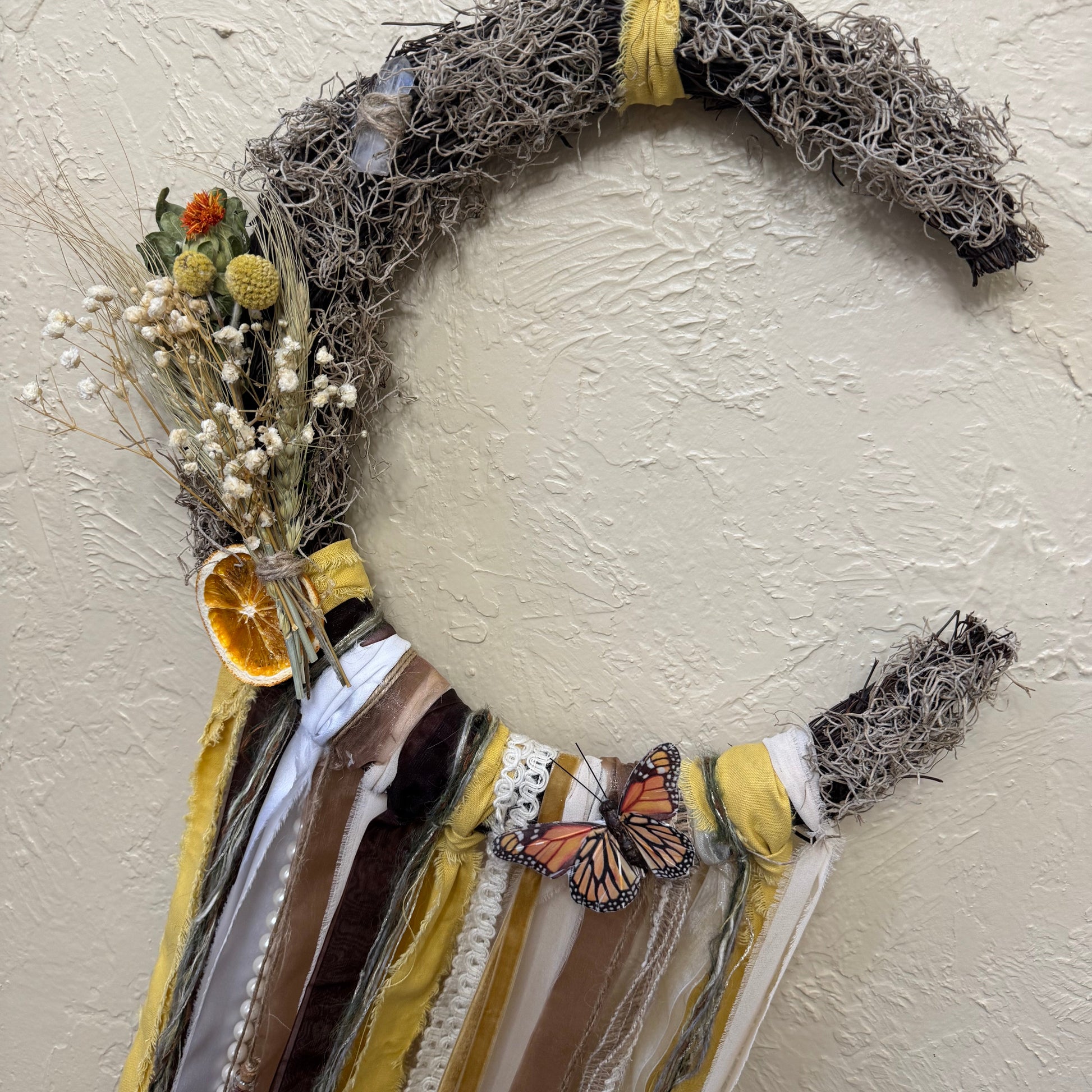 Decorative wreath with natural elements and ribbons on a beige wall
