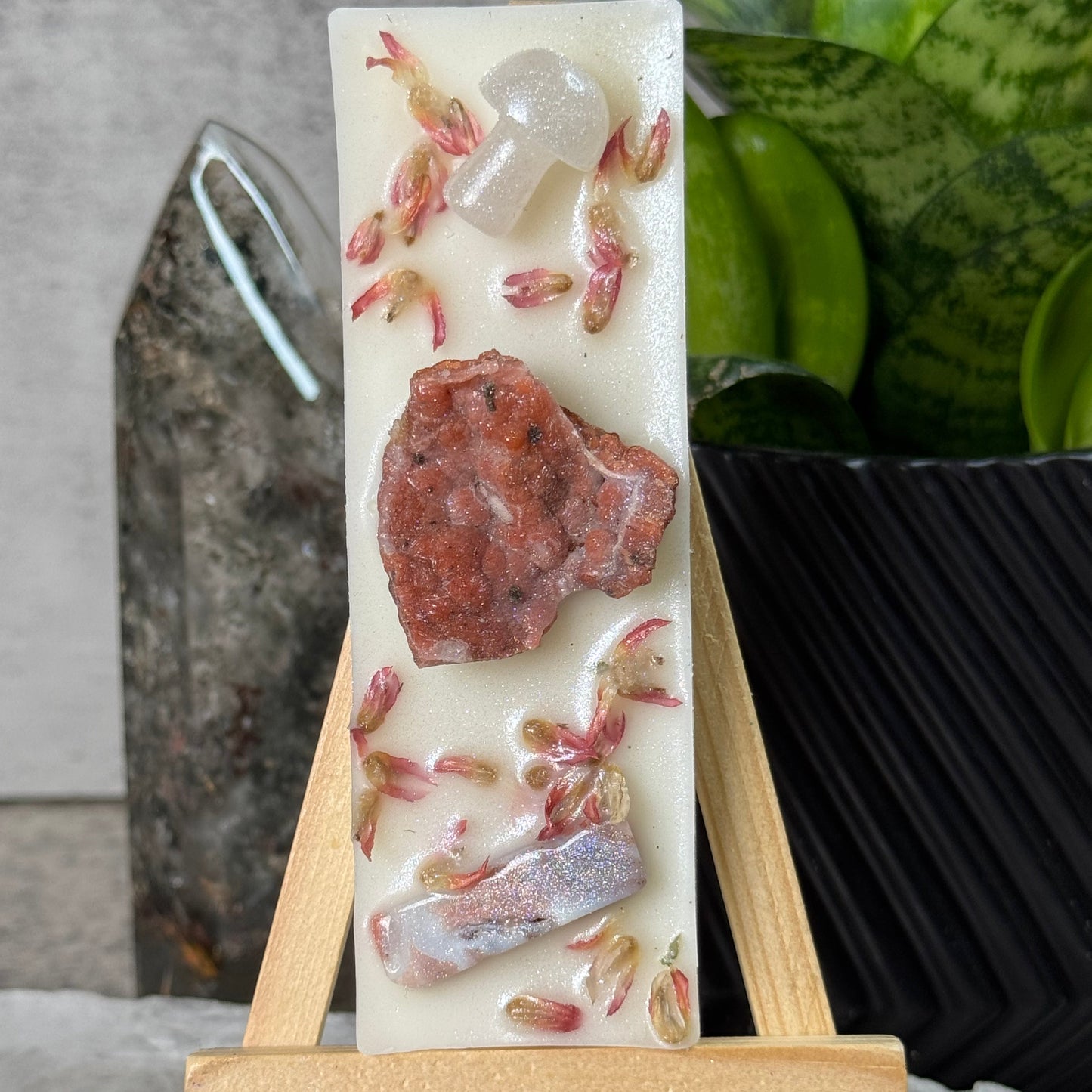 Rectangular soap with embedded natural elements on a wooden stand, set against a blurred background.