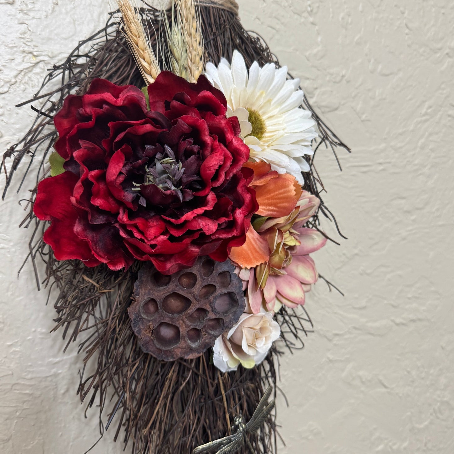 Decorative wreath with red flowers, white daisy, and other elements on a neutral background