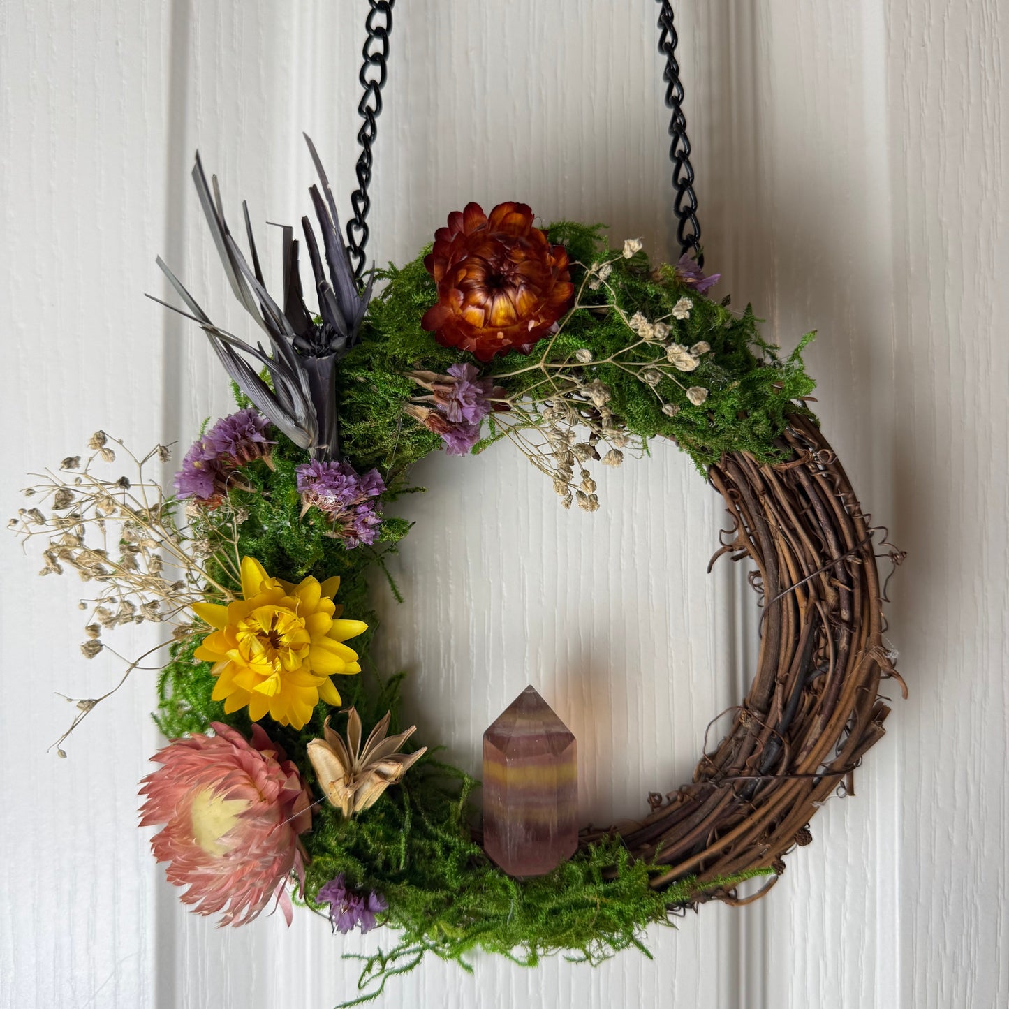 Decorative wreath with flowers and a candle hanging on a white door.