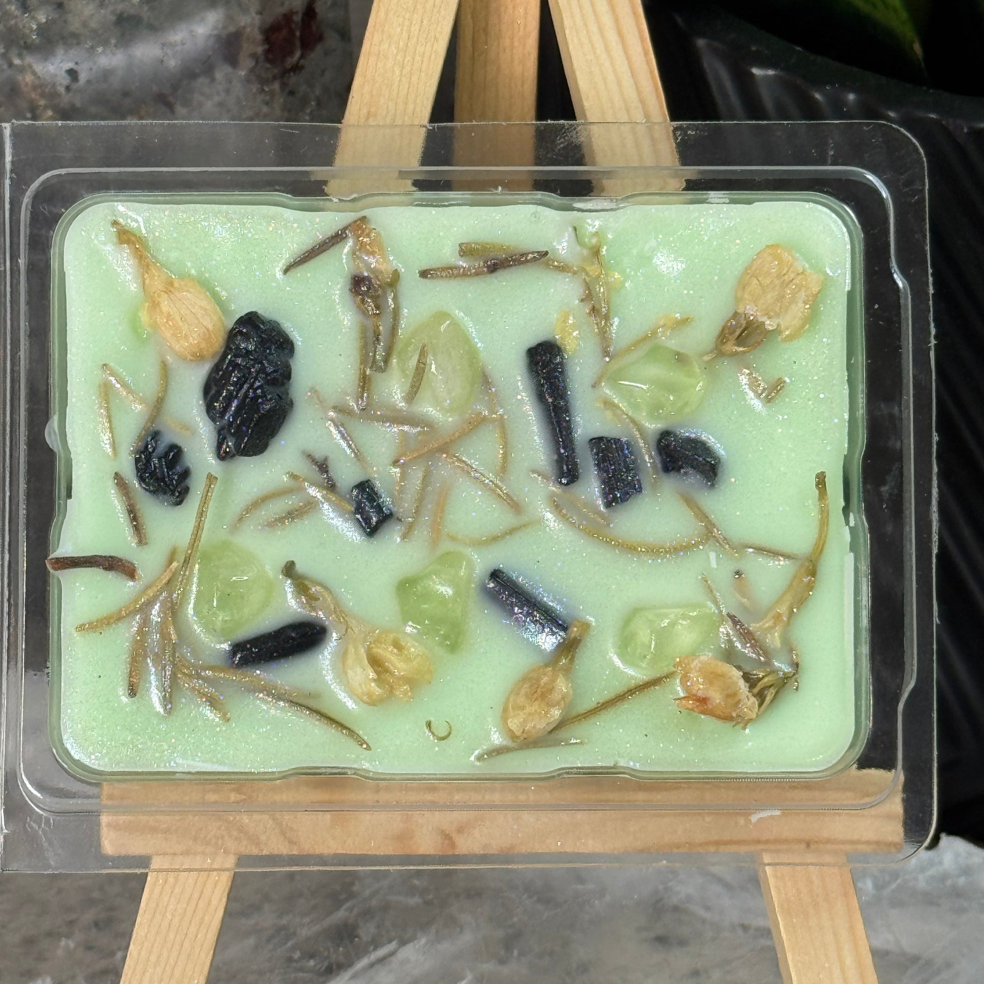 Green soap bar with embedded insects in a clear plastic mold on a stone surface.