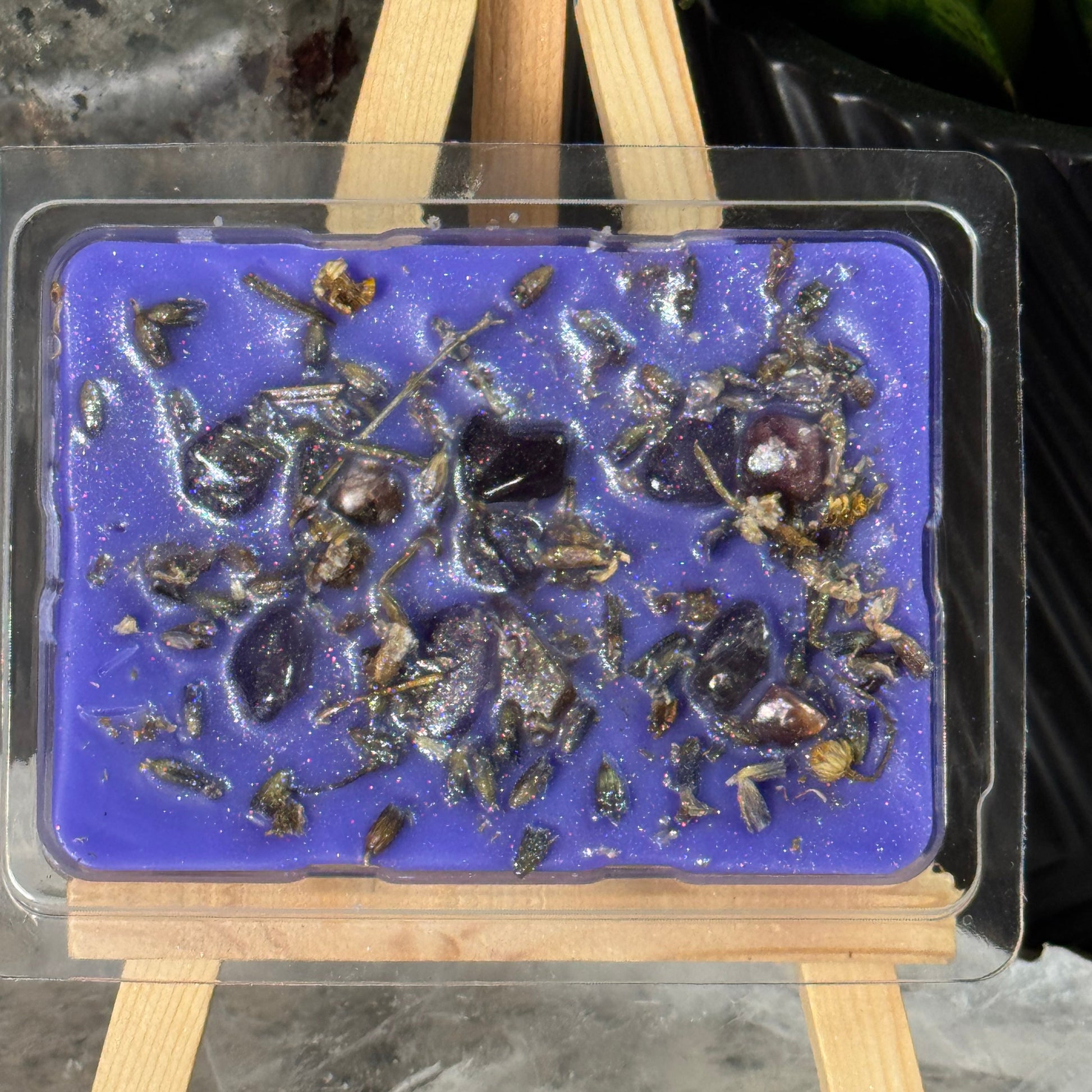 Blue wax mold with embedded stones or crystals in a clear plastic mold on a dark surface.