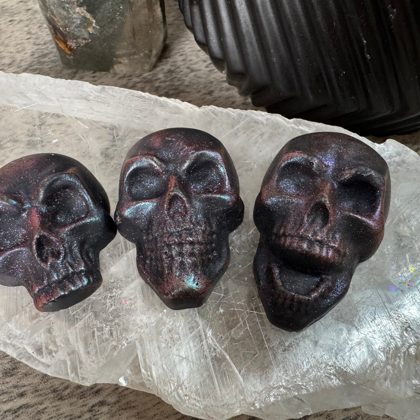 Three dark brown skull-shaped objects on a clear crystal surface.
