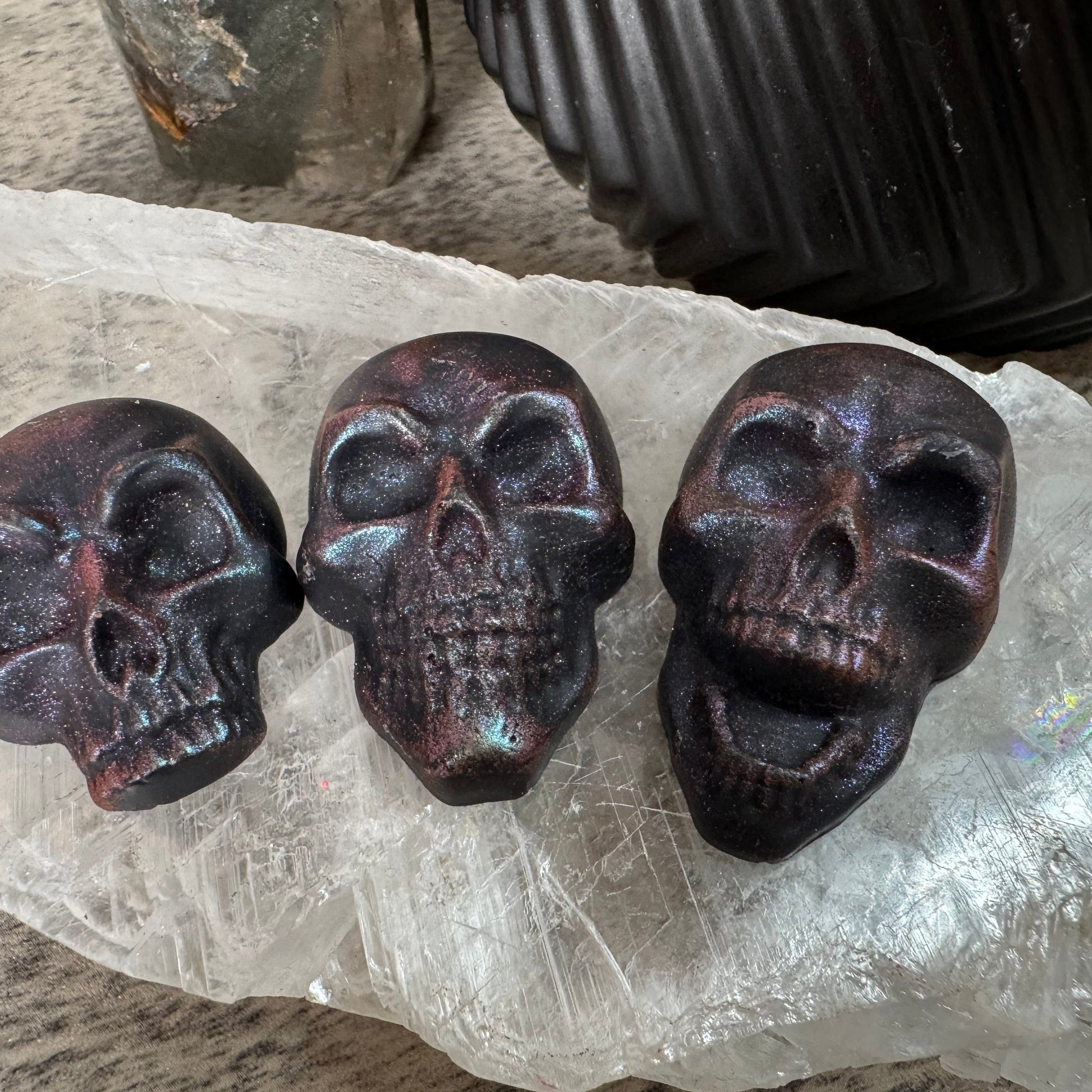 Three dark brown skull-shaped objects on a clear crystal surface.