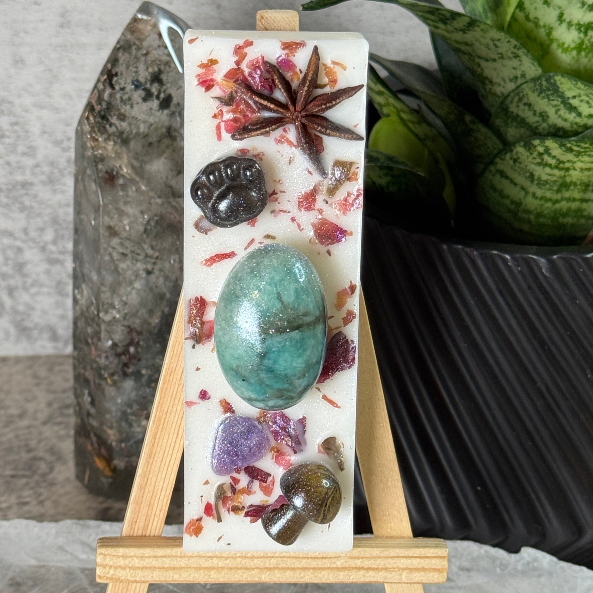 Decorative soap bar with natural elements on a marble stand, set against a stone background.