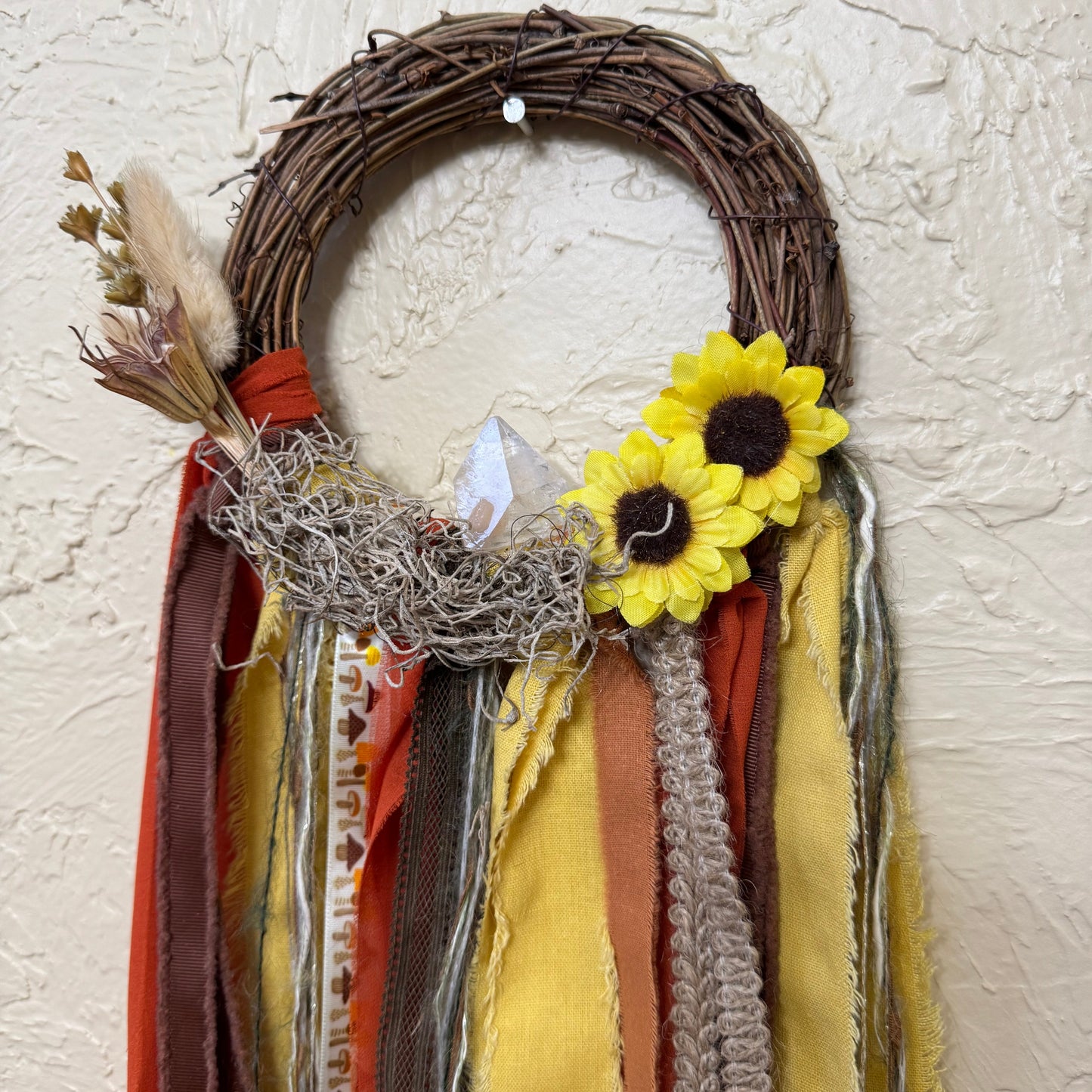 Decorative wreath with sunflowers, ribbons, and twigs on a textured wall.