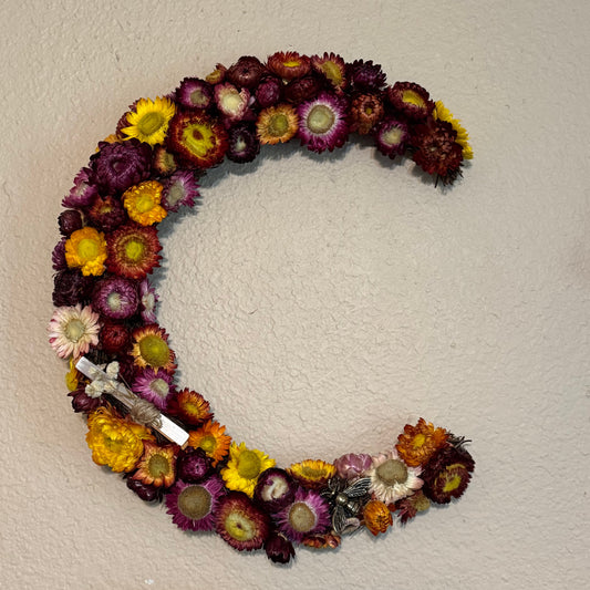 Circular wreath made of multicolored flowers on a plain wall.