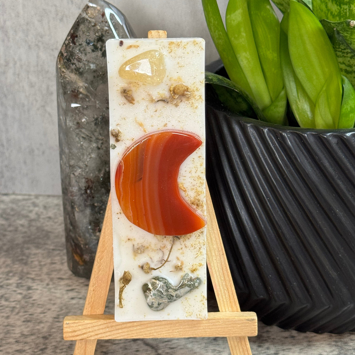 A rectangular carved stone plaque with a crescent moon motif, displayed on a small wooden easel. The plaque has a white base with natural inclusions and a prominent orange-red crescent.