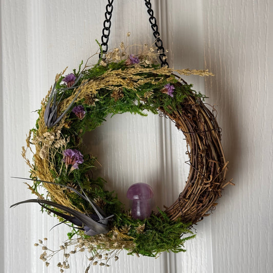 Decorative wreath with greenery, flowers, and a purple ornament on a neutral background