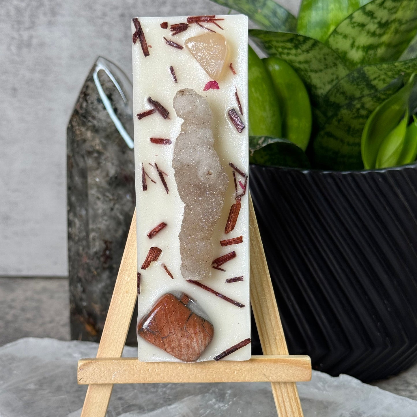 Rectangular soap bar with natural ingredients on a stand, surrounded by greenery.