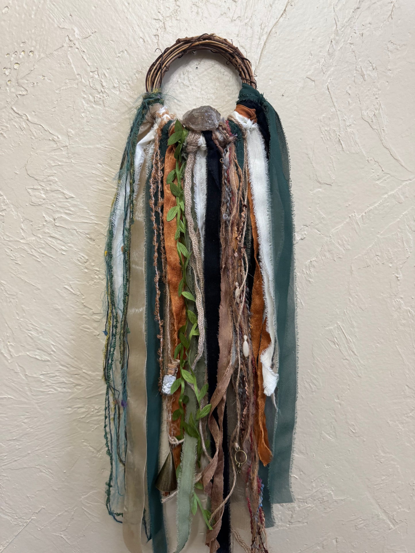 Decorative wall hanging with ribbons and leaves on a textured beige wall