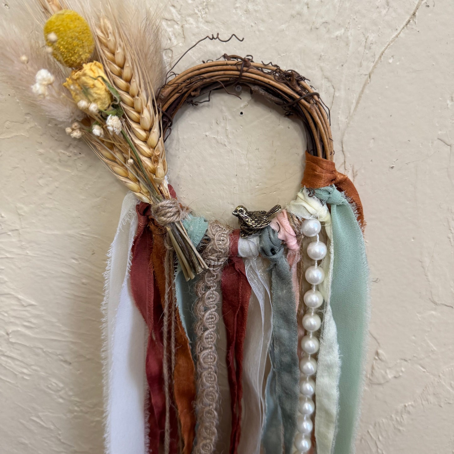 Decorative wreath with ribbons, flowers, and pearls on a textured beige background