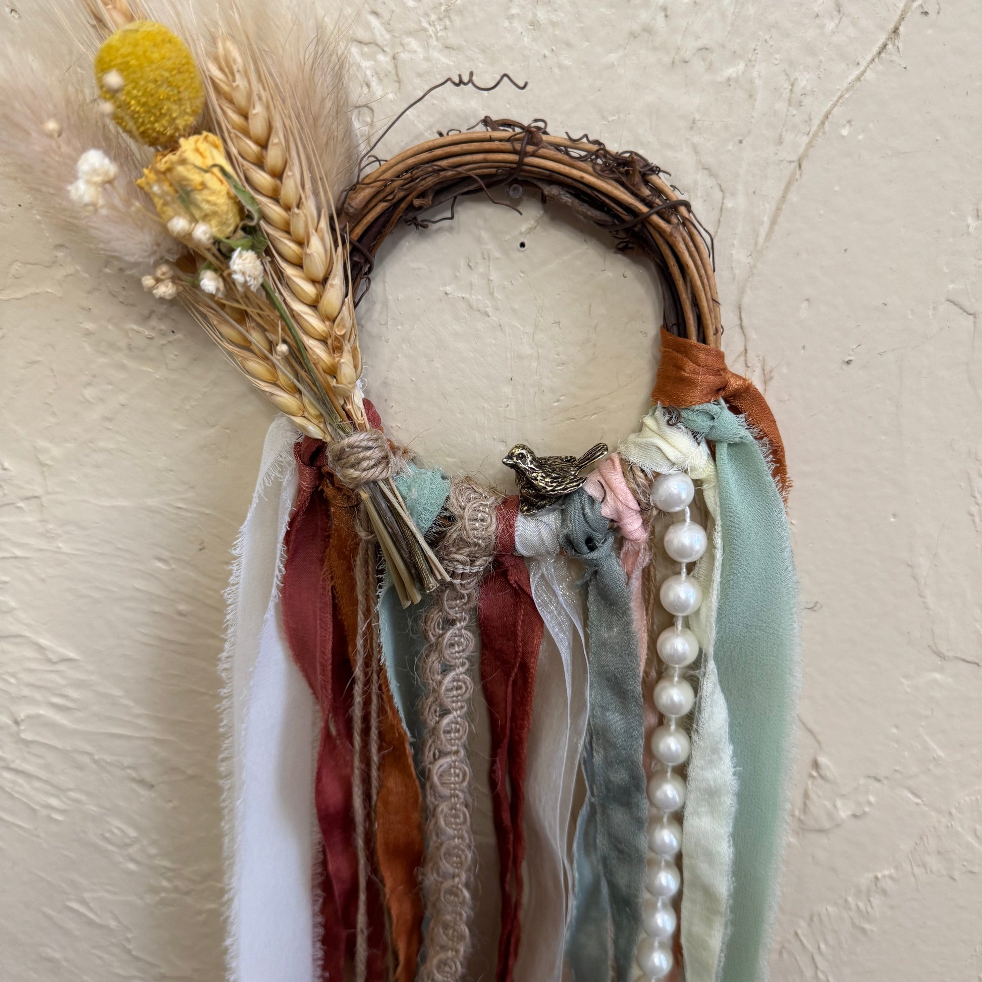 Decorative wreath with ribbons, flowers, and pearls on a textured beige background