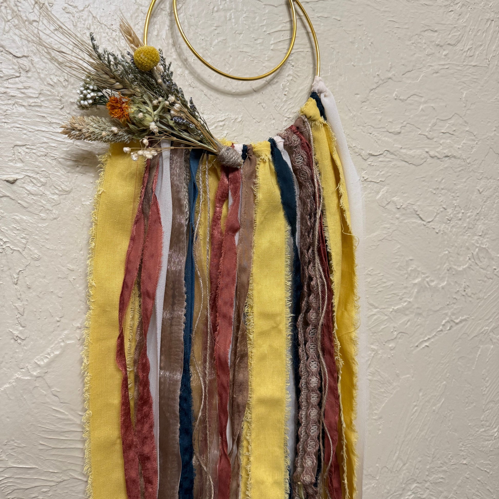 Decorative hanging with ribbons and dried flowers on a textured wall.