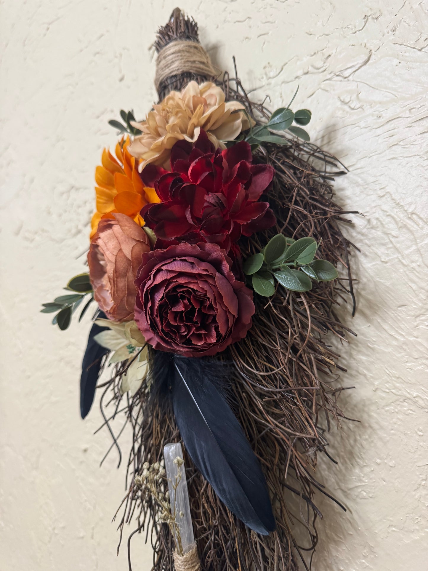 Decorative wreath with flowers and feathers on a textured wall