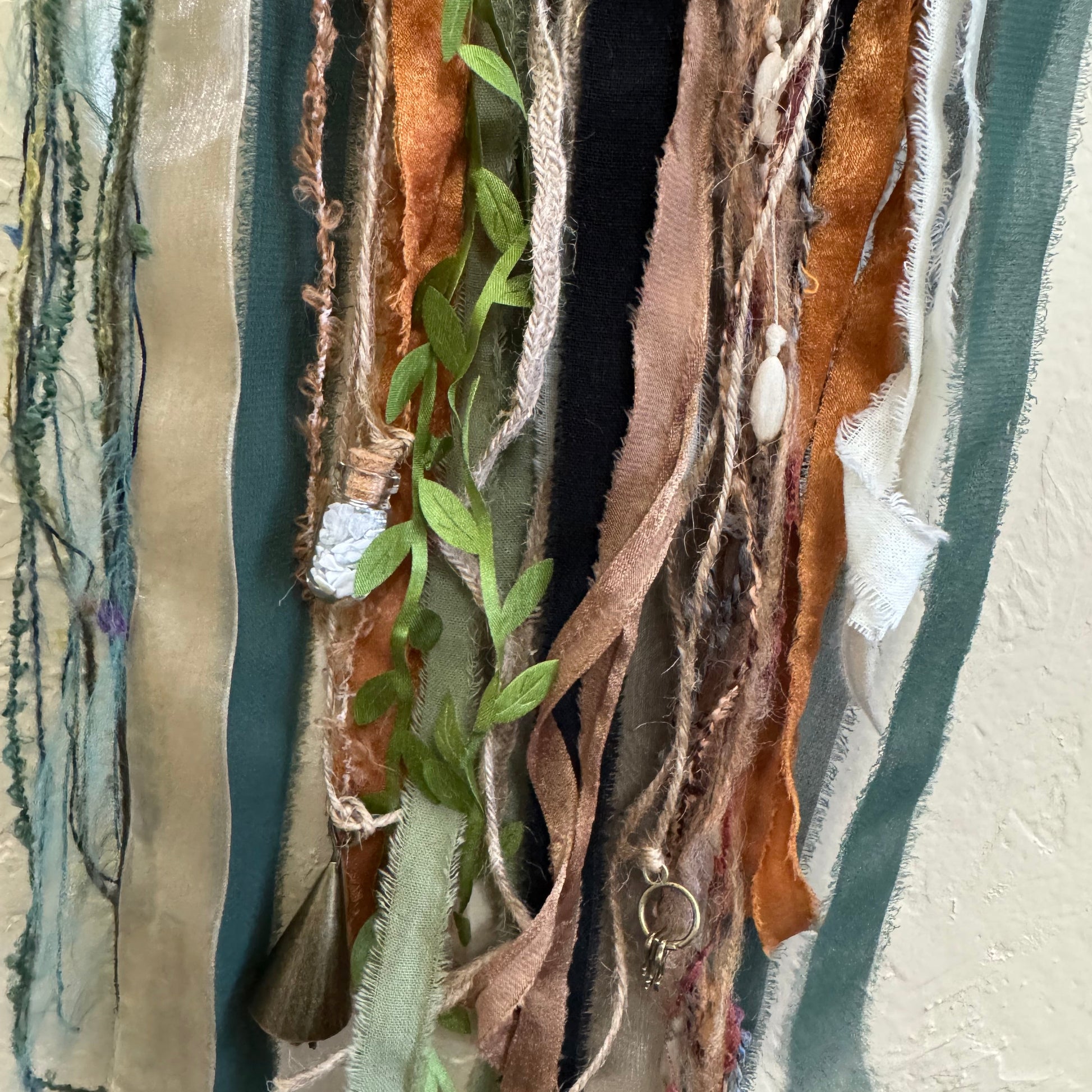 Textile art piece with ribbons and leaves on a textured background