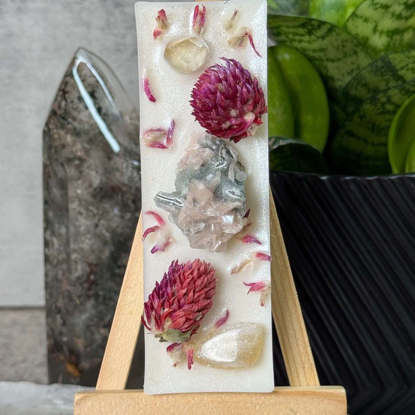 Decorative soap bar with floral and crystal design on a wooden stand, with a plant in the background.