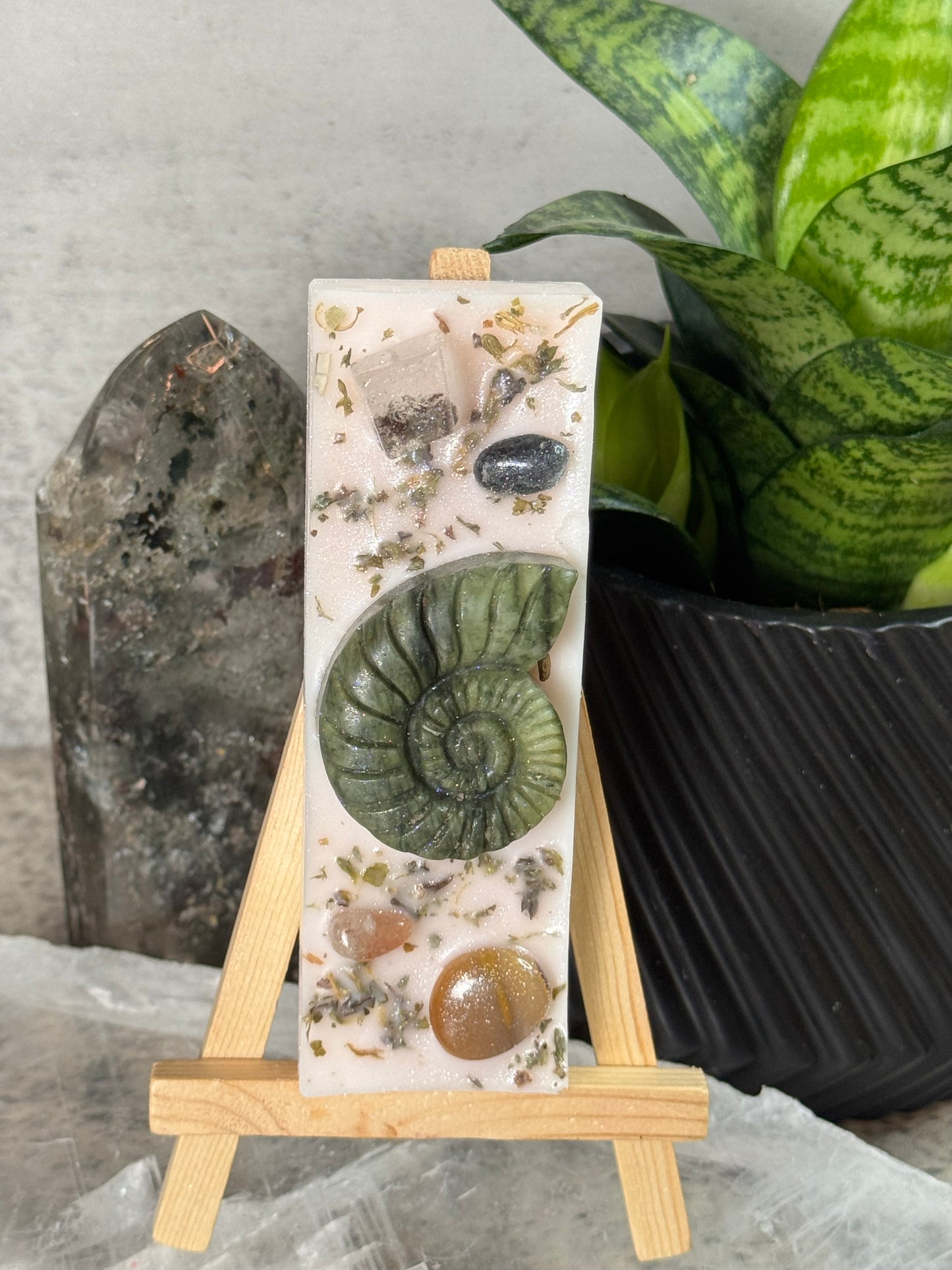 Decorative stone with natural elements on a stand, surrounded by plants and rocks.