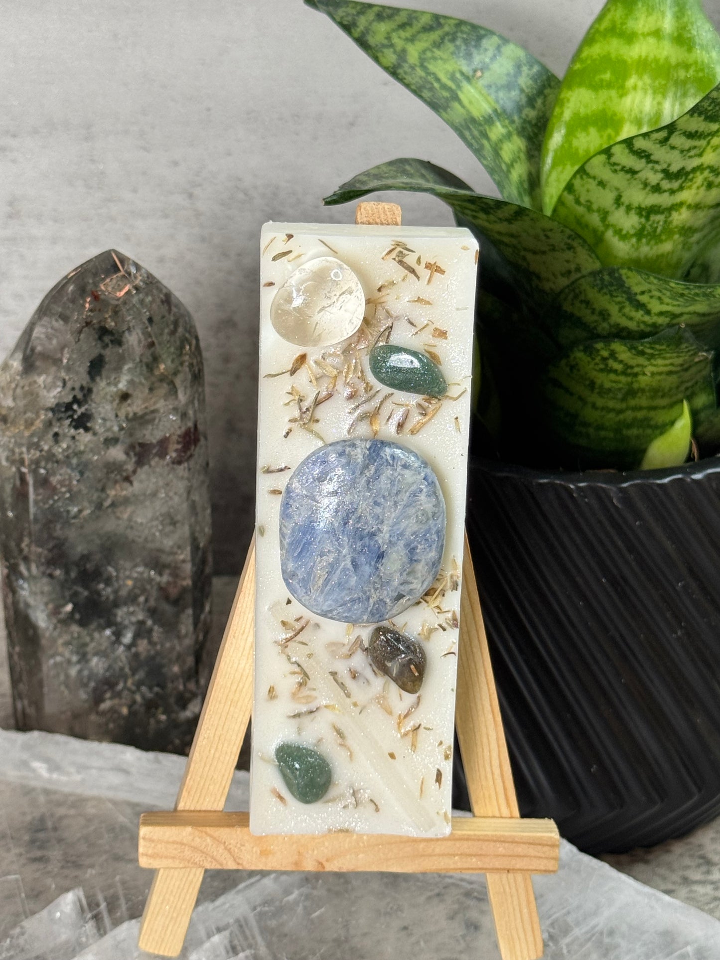 Decorative stone with embedded stones on a wooden stand, with a plant in the background.