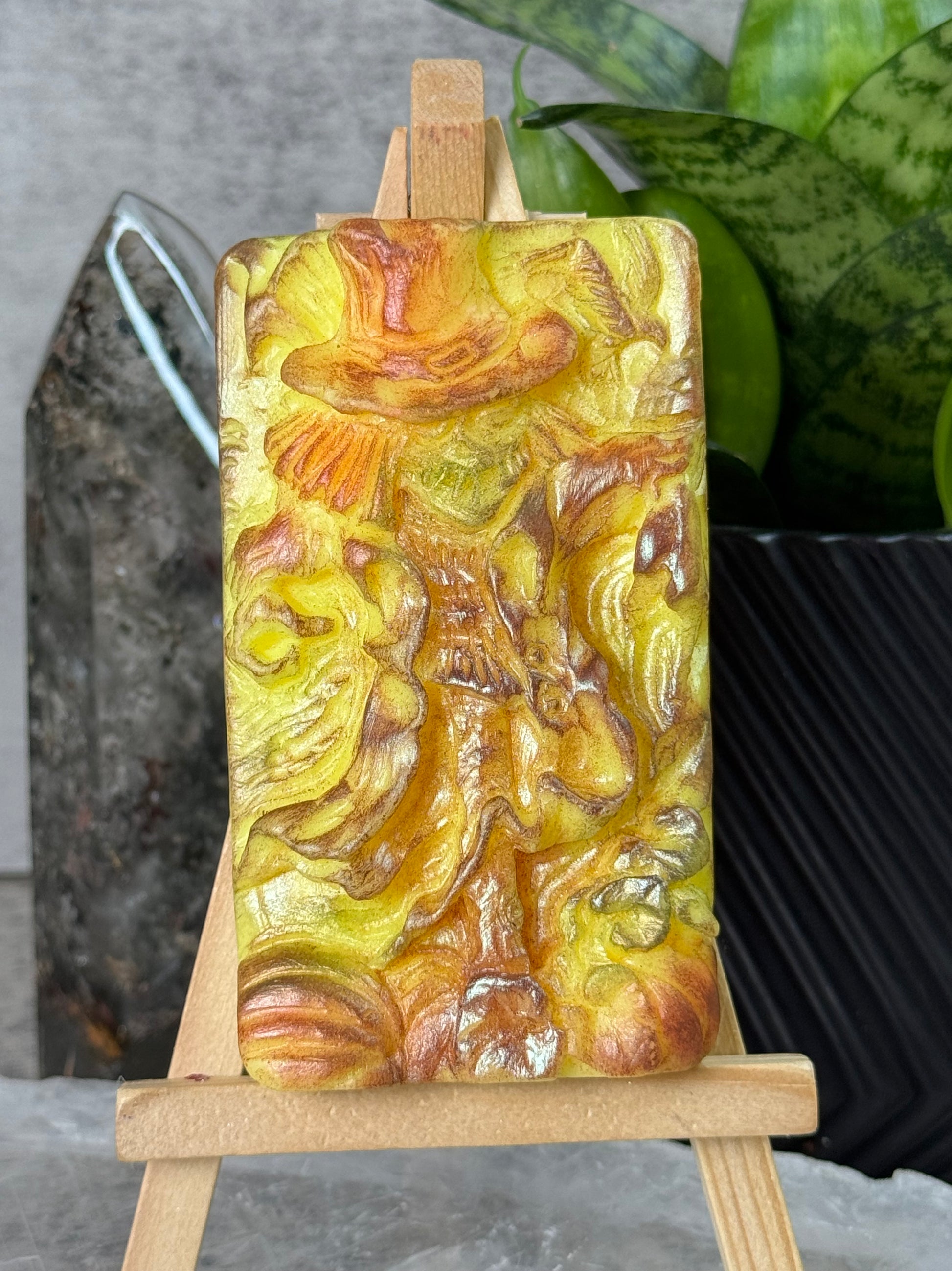 Decorative soap bar with intricate design held by wooden sticks on a gray surface.