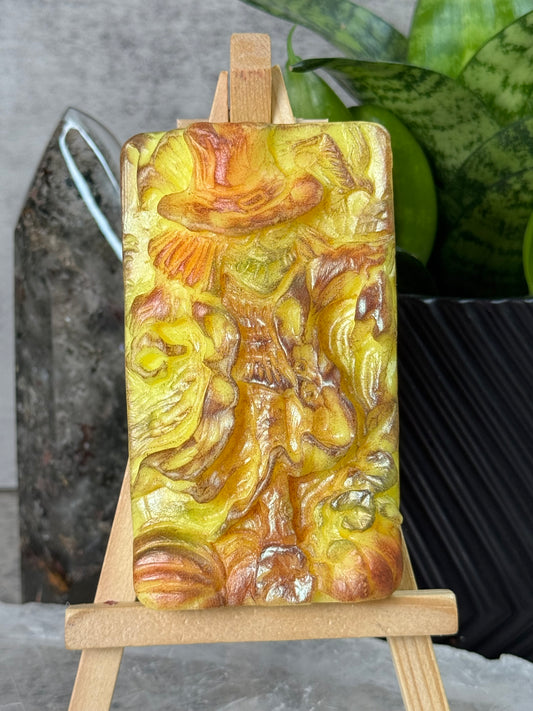 Decorative soap bar with intricate design held by wooden sticks on a gray surface.